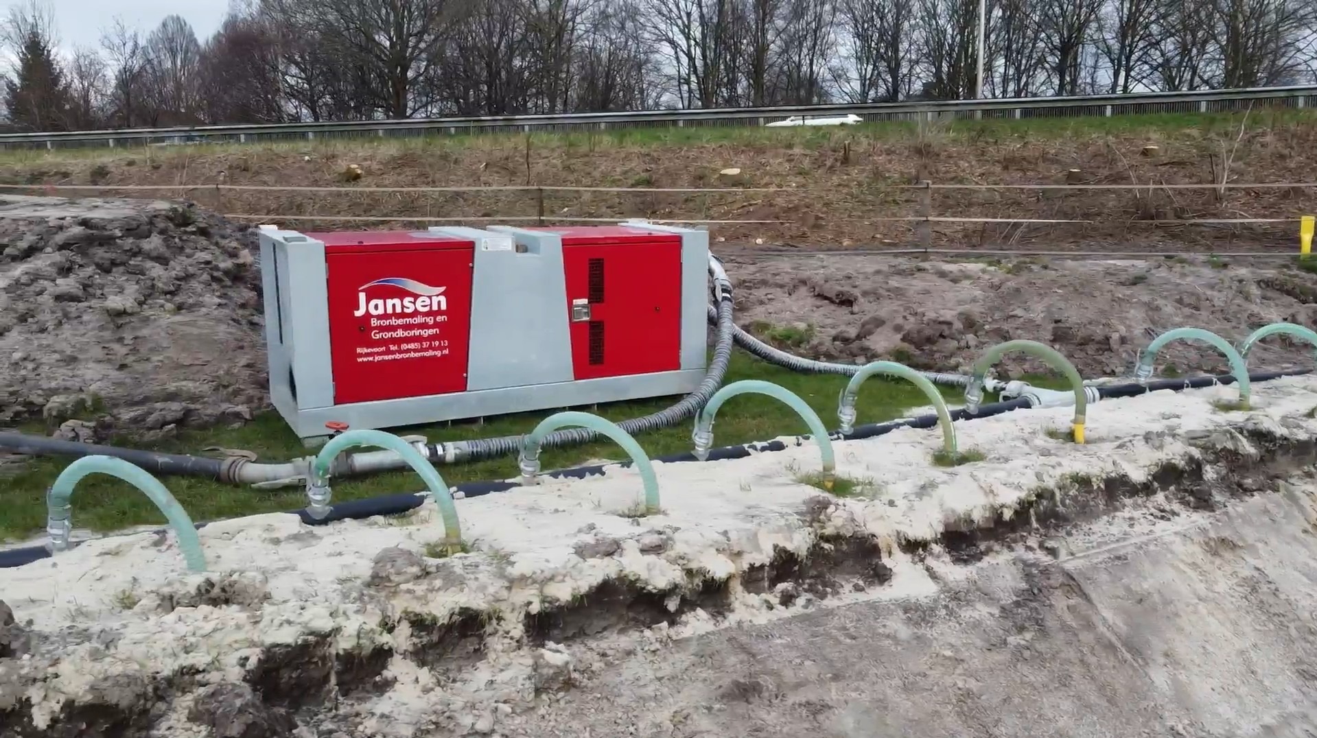 Mobiele bouwplaatsinstallatie met rode Jansen-bronbemaling unit en slangen voor grondwateronttrekking langs een zandige sleuf.