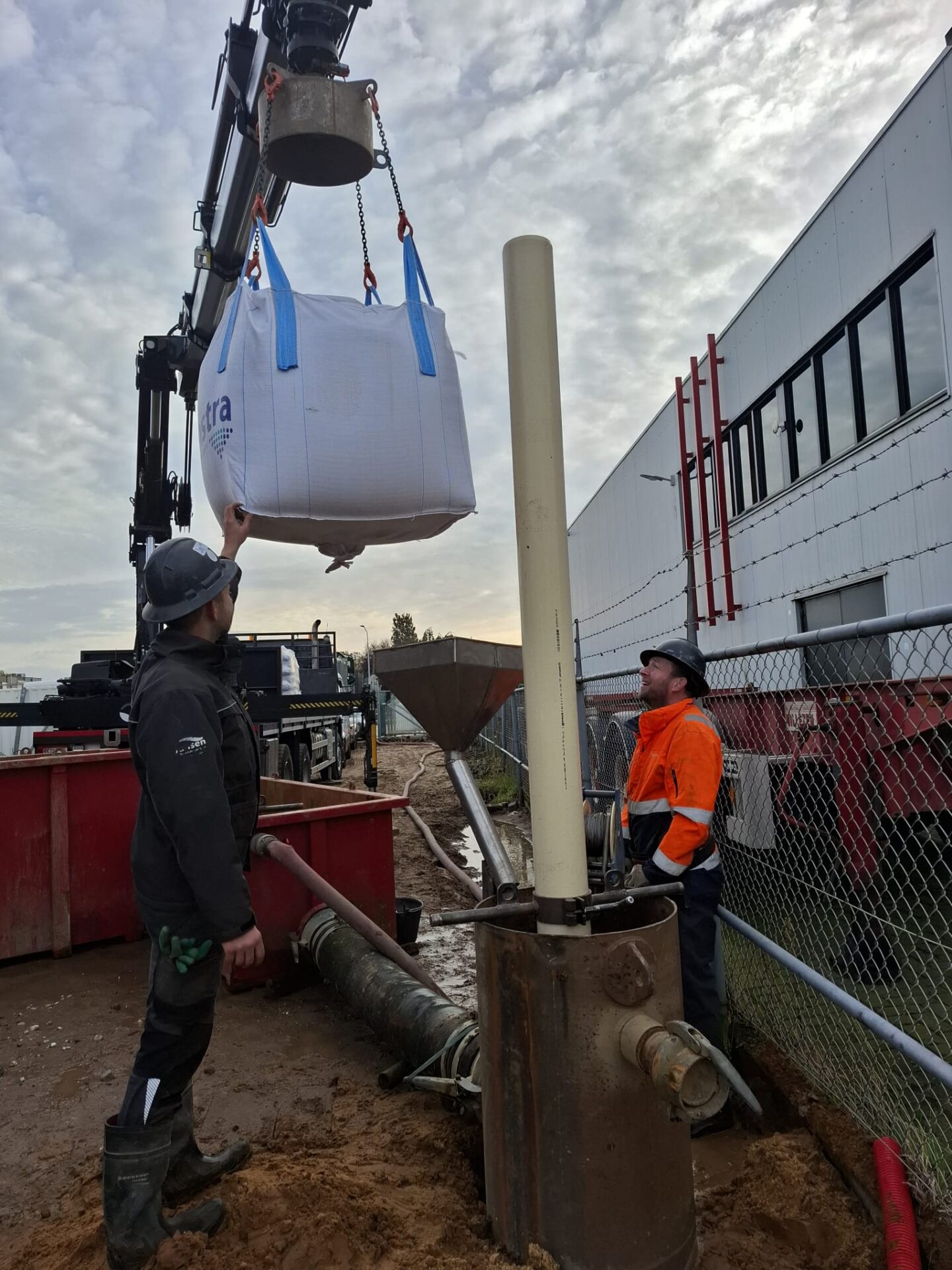 Medewerkers plaatsen met een kraan een big bag filtermateriaal in een ontijzeringsinstallatie als onderdeel van een bronbemalingssysteem.